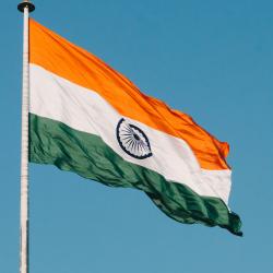 The national flag of India, hoisted at the top of a flagpole, being blown by a strong breeze.